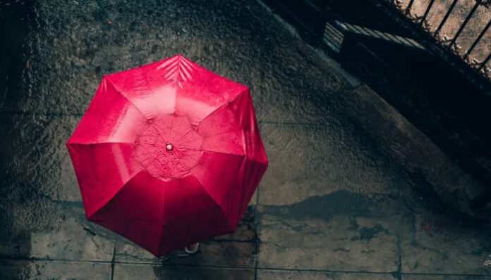Girl with red umbrella standing in the rain for a post about songs about rain